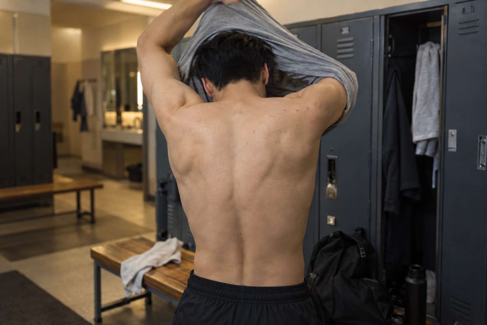탈의실에서 티셔츠를 입으며 드러난 20대 남성의 어깨와 윗등, 작은 붉은 점 몇 개
