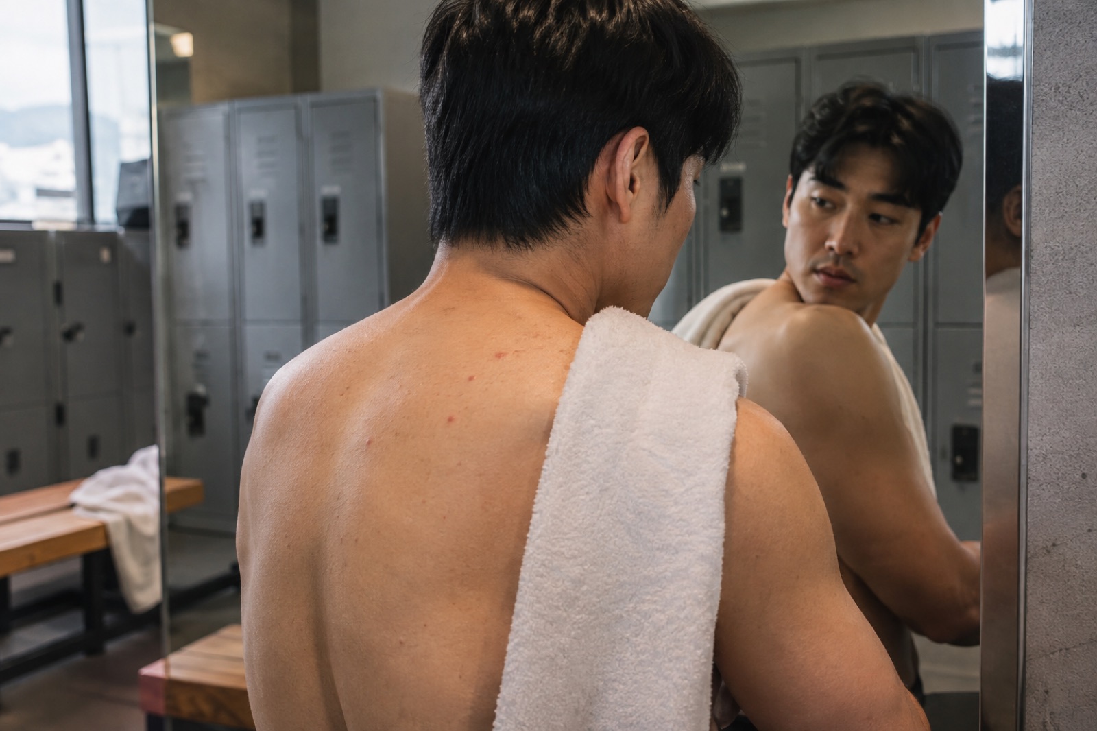 헬스장 탈의실 거울로 어깨 너머 윗등의 작은 붉은 돌기를 살피는 20대 남성